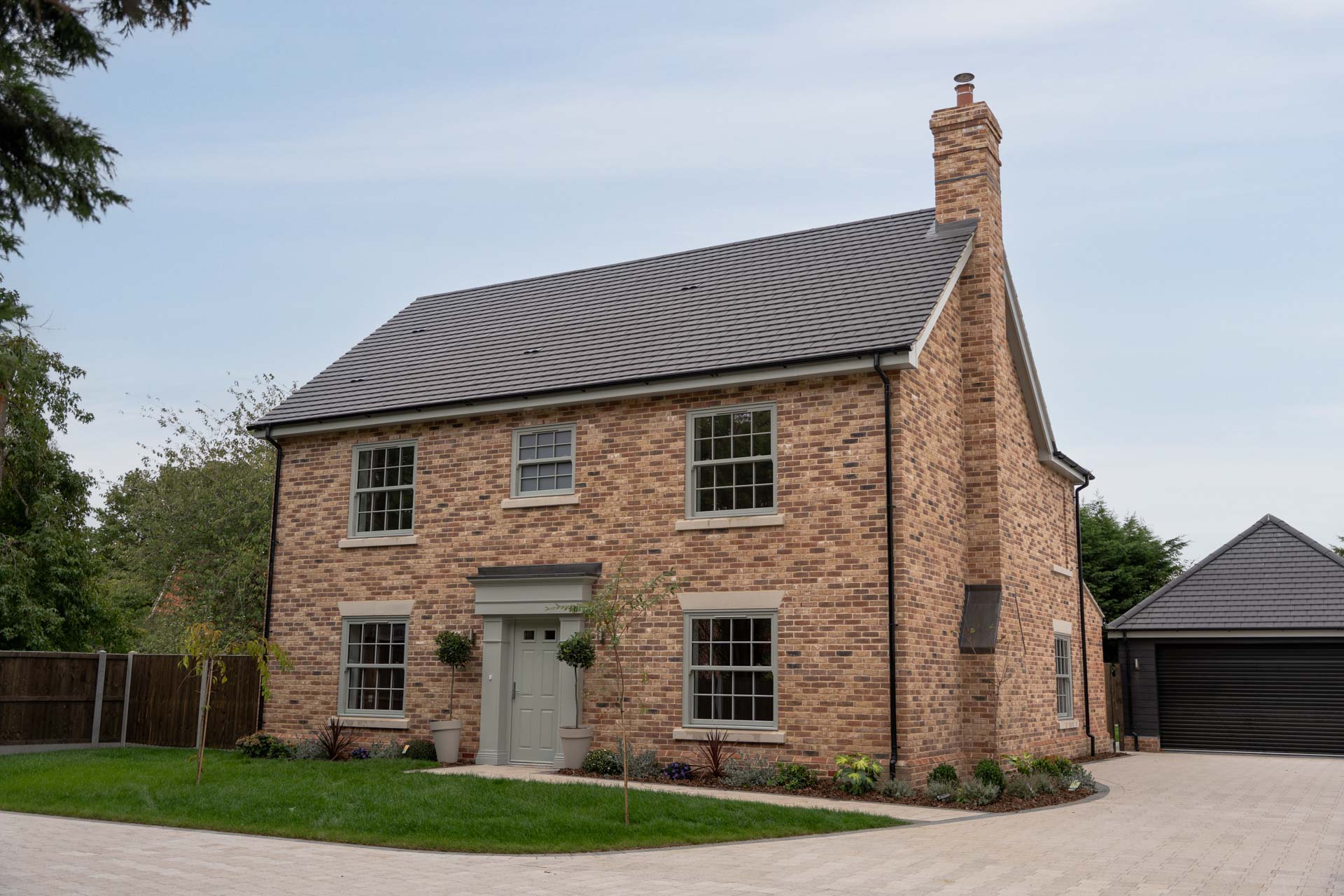 Front elevation of a brick home at Malting Paddocks with sage uPVC vertical sliding windows and a sage composite front door