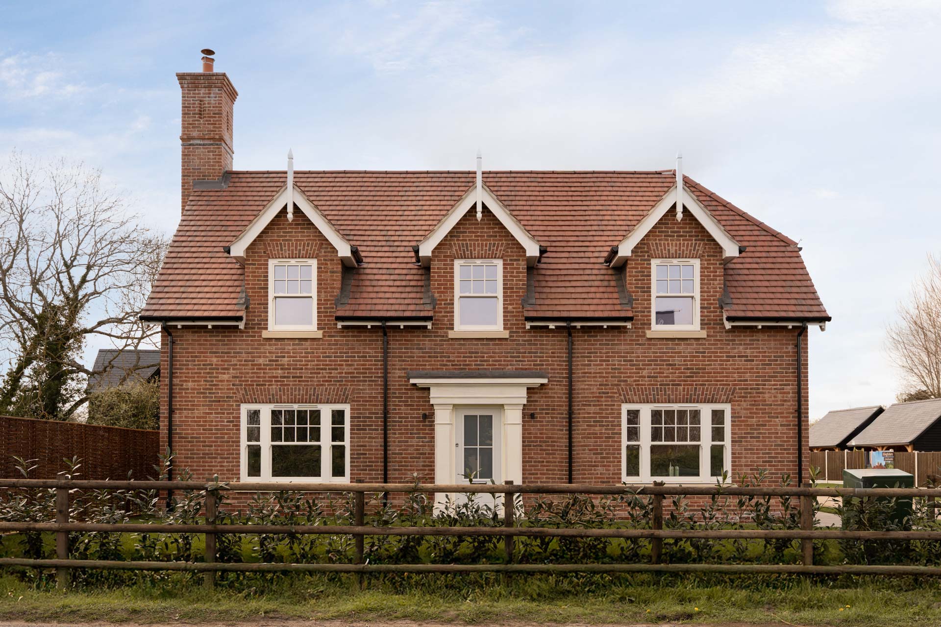 Symmetrical red brick front elevation at The Nest, Abberton, with cream uPVC vertical sliding windows in three dormers and a cream composite front door