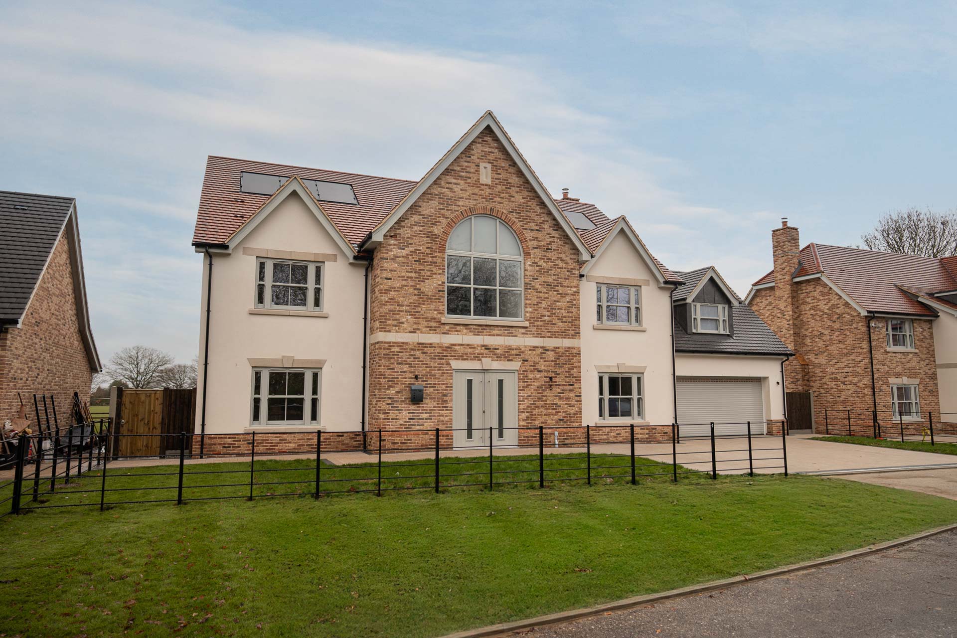 Front elevation of a large brick and rendered home at Ulting Meadows, with sage uPVC vertical sliding windows, an arched feature window and a composite front door